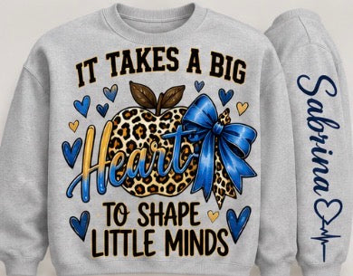 Personalized teacher sweatshirt reading It Takes a Big Heart to Shape Little Minds, with blue and leopard print heart and customizable sleeve name